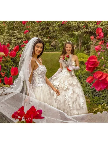 A vibrant outdoor fashion shoot for a collection of Christian wedding gowns. The composition uses the natural frame of bougainvillea flowers to create a romantic, garden-like atmosphere that enhances the elegance of the bridal wear.