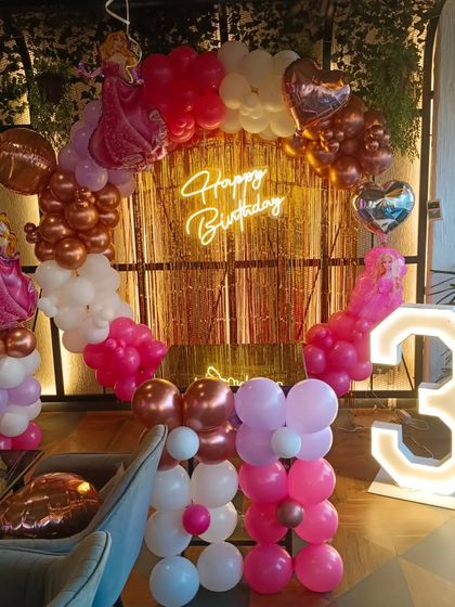 A princess-themed third birthday party. This setup features a circular balloon arch in shades of pink and rose gold, with princess cutouts and a large light-up number '3'.