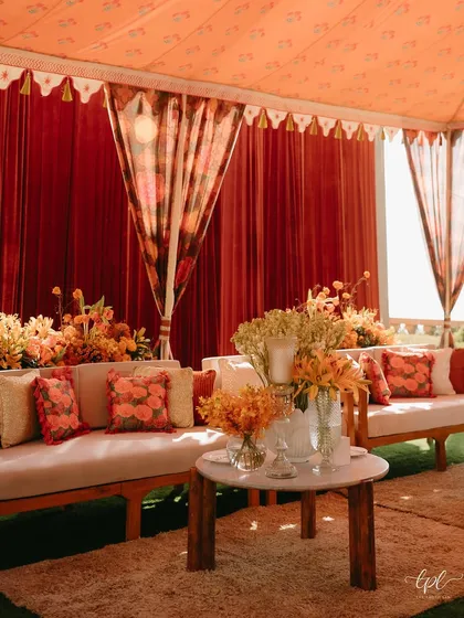 A cozy lounge area at a Mehendi, featuring rich red velvet drapes and custom floral-print cushions. We use textiles and prints to layer textures and colors, creating a warm and inviting atmosphere.