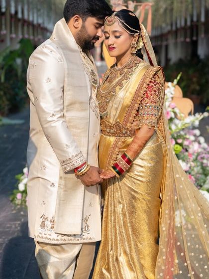 A romantic portrait of the bride and groom. The sheer, embellished veil over her gold saree adds a layer of modern grace to her traditional wedding look.