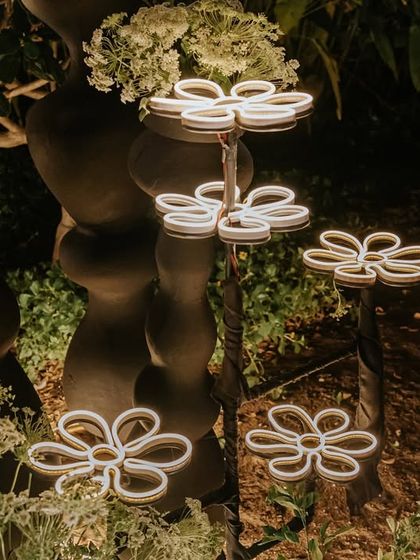 I love incorporating unique lighting elements. These custom-made, whimsical flower-shaped neon lights were placed within the greenery to add a magical, playful glow to the engagement party entrance.
