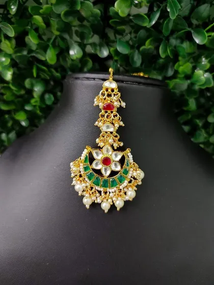 A lovely crescent-shaped maang tikka with a floral kundan motif and red and green stones.