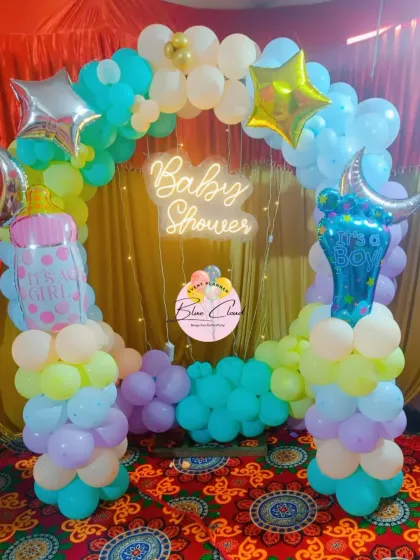 A pastel-themed baby shower or gender reveal setup with a neon sign and pillars for 'It's a Girl' and 'It's a Boy'.