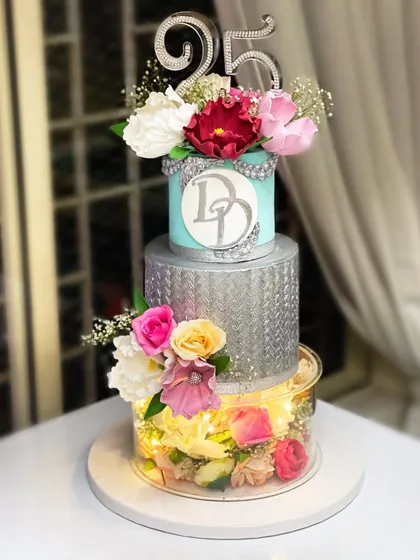 Celebrating 25 years of love with this stunning silver anniversary cake. It features a lit-up separator tier filled with flowers, silver stenciling, and a custom monogram, combining my signature ganache with fresh and sugar flowers.