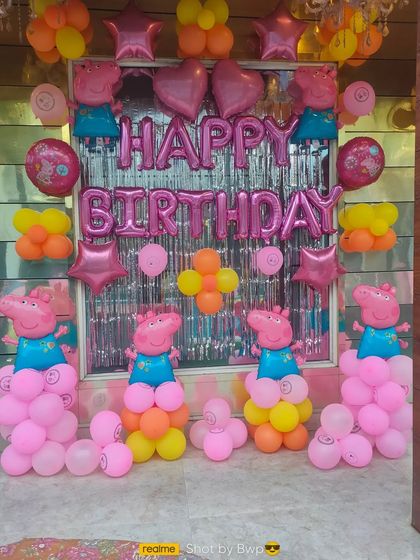 A fun Peppa Pig birthday setup with character balloon sculptures, pink foil "Happy Birthday" letters, and a silver foil curtain.