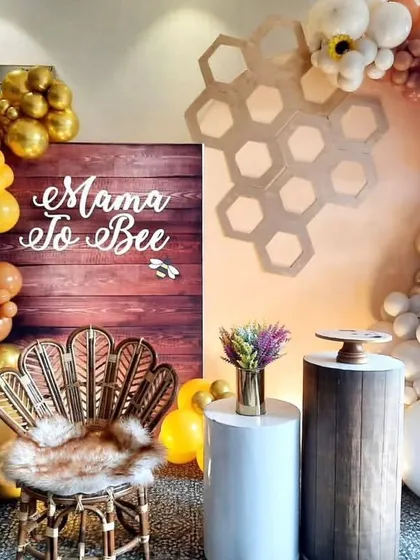 A chic and modern "Mama to Bee" baby shower setup, featuring a stylish peacock chair, a rustic wooden backdrop, and a beautiful balloon arch in warm, earthy tones.