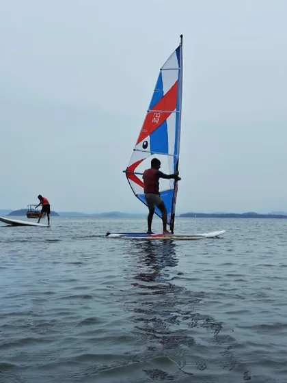 A windsurfer and a paddleboarder share the water, enjoying a calm day at our Karwar training center.
