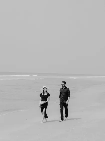 A minimalist black and white photograph of the couple walking on the beach. The simplicity of the composition puts all the focus on them and the serene environment.