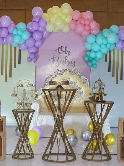 This "Oh Baby" backdrop in pastel colors is perfect for a baby shower. The setup includes decorative birdcages, wooden fences, and elegant tables for gifts and desserts.