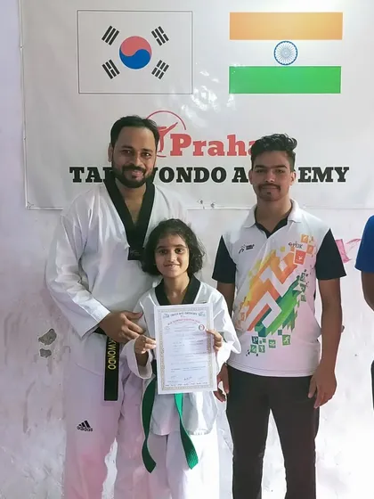 A young green belt student with her certificate, flanked by her proud coaches.
