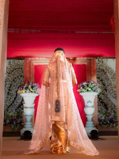 The bride makes her grand entrance. The back view shows the full length of her sheer veil and the intricate design of her blouse, creating a breathtaking moment.