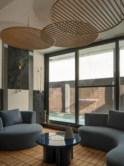 A view pavilion overlooking a water body serves as an informal lounging space. The room features curved blue sofas and sculptural wooden ceiling panels, creating a tranquil retreat.