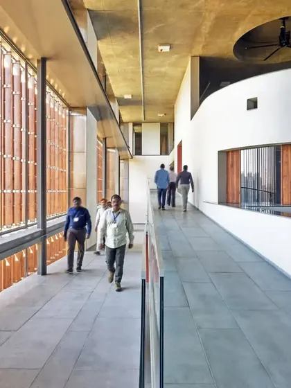 A wide, light-filled corridor at the JSW School of Public Policy at IIM Ahmedabad. The extensive use of glass and terracotta jaalis allows for natural light and ventilation while framing views of the surrounding campus.