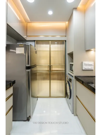 This modular kitchen features a sleek, contemporary design with smart storage solutions. The gold-trimmed glass doors of the utility area add a touch of elegance and separation.