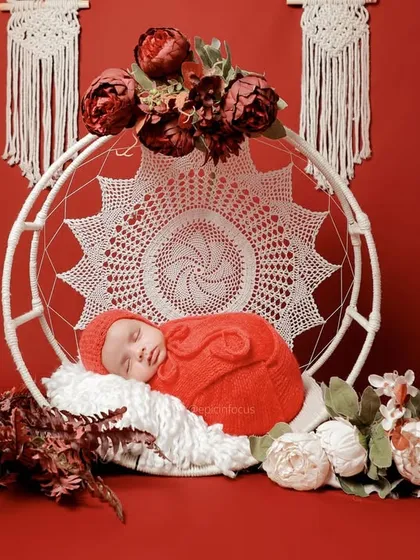A striking setup with a baby in a vibrant red swaddle, resting in a white macrame swing against a bold red background.