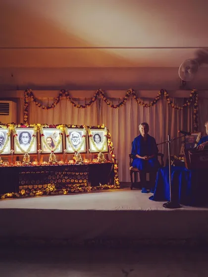 Nayaswami Jyotish and Devi on stage during a satsang, with the beautifully decorated altar of masters beside them. Their presence brings a special blessing to our gatherings.