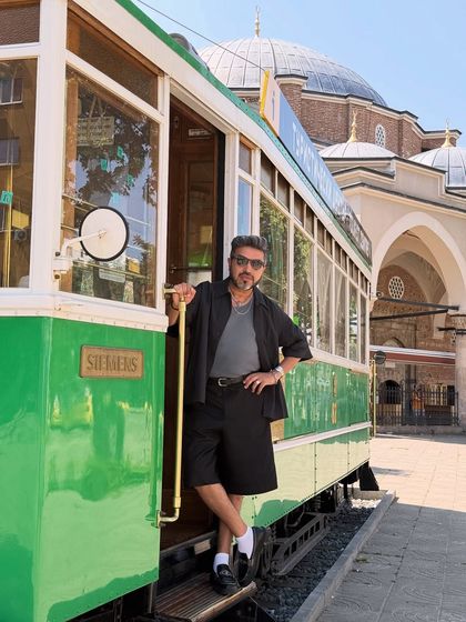 Posing by a vintage tram in Sofia, Bulgaria. My outfit is a study in monochrome, with a black open shirt, grey tee, and black shorts, perfect for a stylish day of exploring.