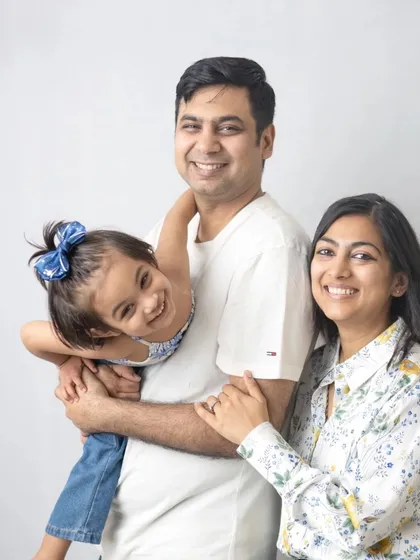 A playful family portrait against a simple white background. The daughter's happy, upside-down pose adds a touch of fun and personality.