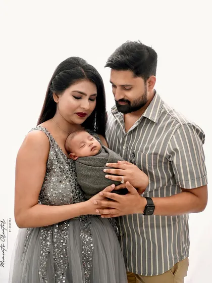 A classic and tender family portrait. The parents hold their sleeping newborn, creating a timeless image of love and new beginnings in a simple, bright studio setting.
