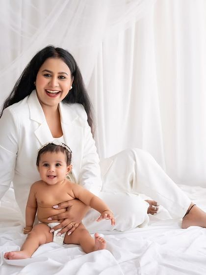 A joyful portrait of a mother and her baby, both dressed in white.