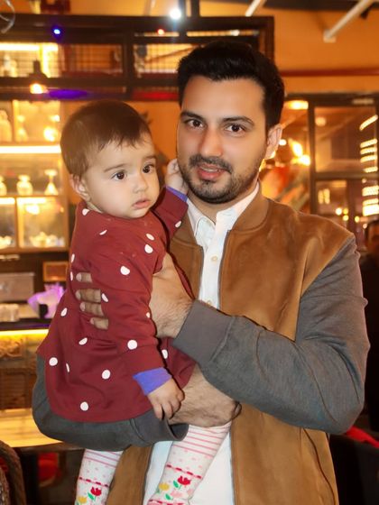 A father holds his young baby, who looks on with a curious expression. A simple, beautiful father-child portrait.