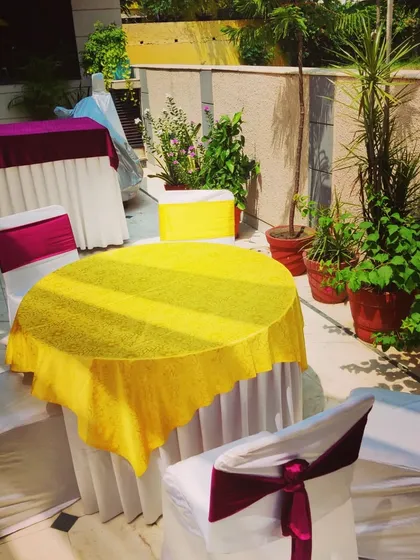A simple and practical seating arrangement for a home function, with chairs and tables covered in bright yellow and maroon fabric.