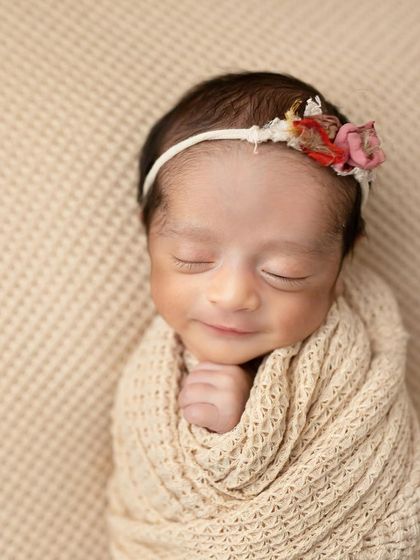 A sweet newborn smile captured in a moment of sleep. Wrapped in a neutral-toned swaddle with a tiny floral headband, this image is the definition of peaceful.