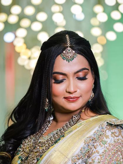 A close up portrait of the bride, highlighting her flawless makeup and the detailed embroidery on her blouse. The green tones of her jewelry perfectly match her saree.