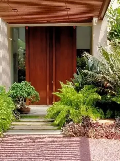 The entrance to the "House in the Hills" is a journey through nature. We used dense ferns, palms, and a bonsai tree to create a vibrant, green pathway that leads to the front door, immediately setting a tranquil tone.