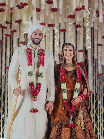 The official portrait of the newlyweds. The couple stands hand-in-hand against the intricately designed floral backdrop, a beautiful symbol of their new beginning.
