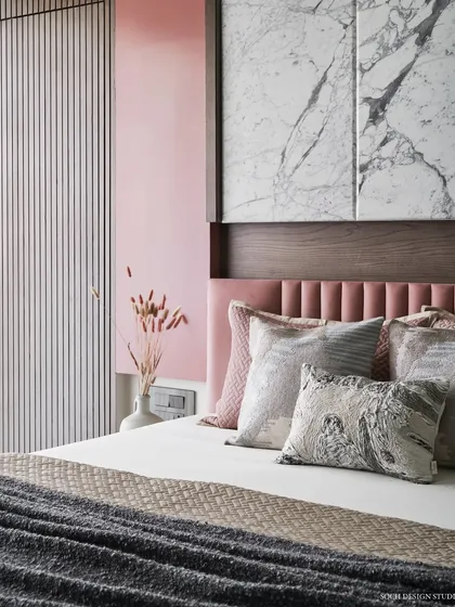 A close-up of the master bed, showing the mix of textures from the plush pink headboard, Satvario marble panel, and dyed ash grey wood. The layered cushions add to the cozy and inviting feel.
