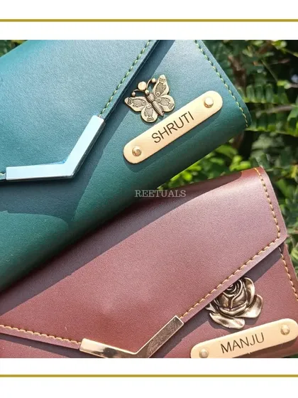 A close-up of the custom-named wallets, one in green with a butterfly charm and one in brown with a rose charm. A perfect personalized birthday gift.
