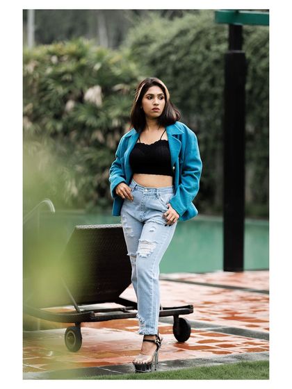 An outdoor fashion shot with a cool, edgy vibe. The blue jacket, black crop top, and ripped jeans create a stylish, modern look.