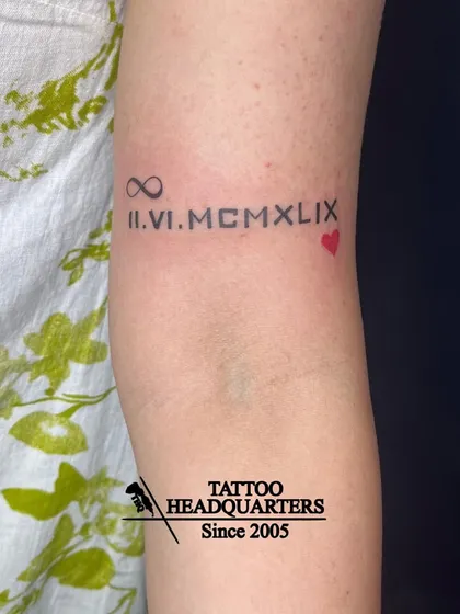 A special date, "II.VI.MCMLIX" (June 2, 1959), tattooed in Roman numerals, with an infinity symbol and a small red heart.