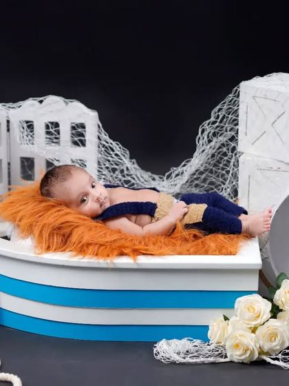 Ahoy, little sailor. This nautical-themed setup features a baby boy in a boat prop, complete with an anchor detail and fishing nets for a charming maritime feel.