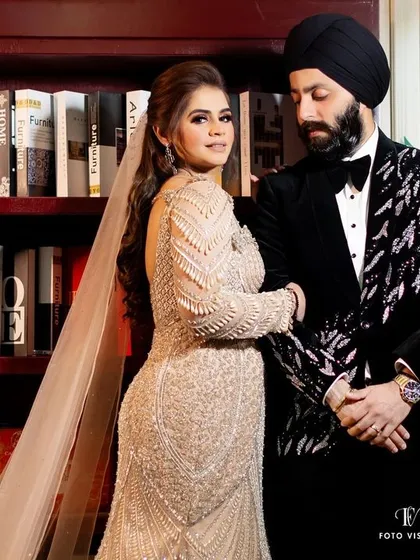 A sophisticated portrait of the couple in a library setting, her long veil adding a touch of bridal elegance to the modern pose.