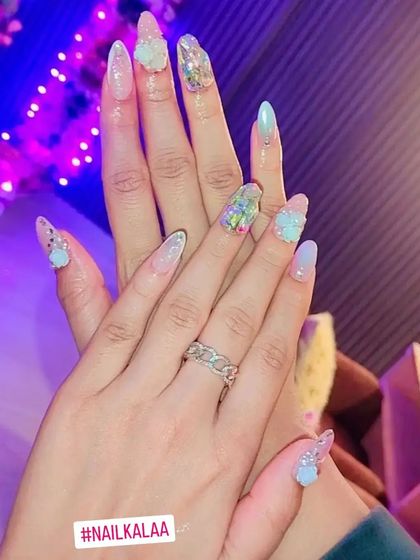 A dreamy, ethereal nail set with a mix of iridescent finishes, glitter, and delicate 3D floral and pearl accents.