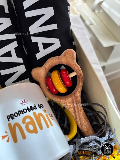 A peek inside a 'Promoted to Nani' hamper, showing the custom mug and a classic wooden baby rattle. I focus on including items that are both sentimental and useful.