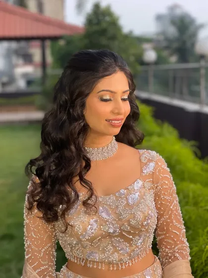 Dazzling and ready for her Sangeet. This look features a beautiful golden glitter eye, flawless skin, and soft, open curls, finished with a sparkling bow hair accessory for a touch of playful glam.