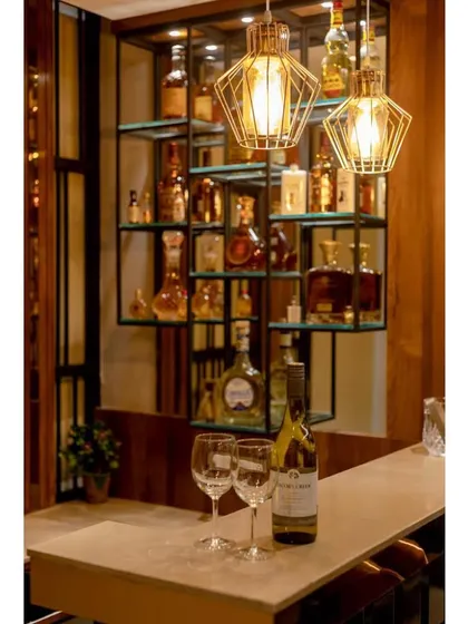 A close-up of the custom metal and glass shelving unit, which elegantly displays the liquor collection. The geometric pendant lights add a final touch of industrial-chic style.