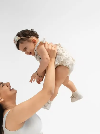 A mother joyfully lifts her baby in the air. The baby's delighted expression and the mother's smile make this a perfect capture of pure happiness.