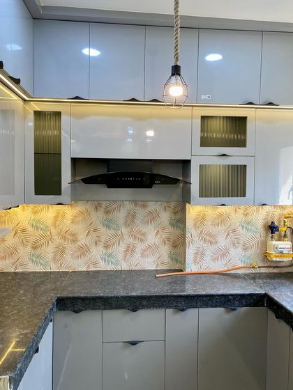 This kitchen features a unique backsplash with a leaf pattern, complementing the grey cabinets and fluted glass shutters.