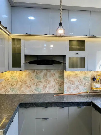 This kitchen features a unique backsplash with a leaf pattern, complementing the grey cabinets and fluted glass shutters.