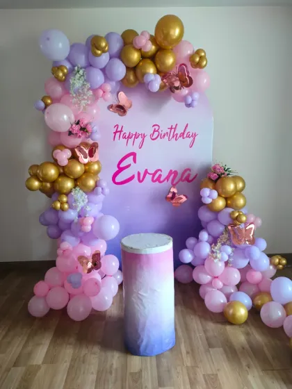 A beautiful butterfly-themed birthday setup with a custom printed backdrop and a pastel balloon garland. A matching plinth is ready for the cake.