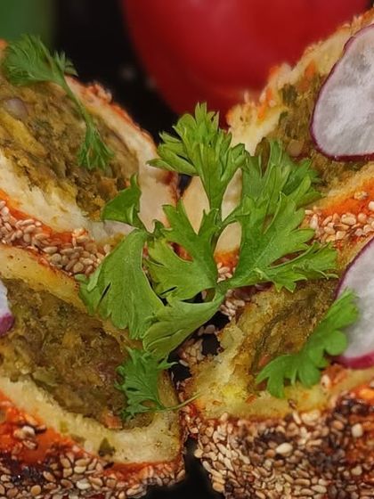 A savory stuffed bread roll, coated with sesame seeds and baked until golden. The cross-section reveals a delicious green filling, showcasing the surprise inside.