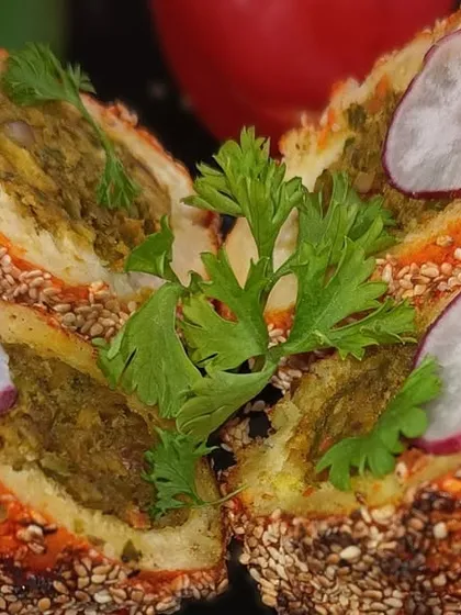 A savory stuffed bread roll, coated with sesame seeds and baked until golden. The cross-section reveals a delicious green filling, showcasing the surprise inside.
