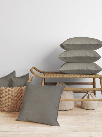 A beautifully styled shot of the grey cushions stacked and placed in a basket, ideal for a catalogue or website banner.