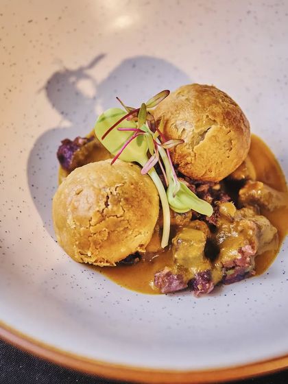 A beautifully plated version of litti chokha. Here, feta and amaranth puff "litti" are served on a bed of purple potato chokha and drizzled with artisanal ghee, elevating a rustic dish to gourmet heights.
