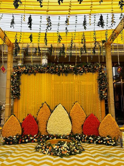 A wide view of the yellow-themed Haldi stage, showing the full setup with the floral backdrop, chevron flooring, and hanging decorations.