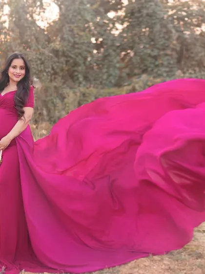 A dramatic outdoor shot featuring a vibrant pink gown with a long, flowing train tossed in the air. This adds a dynamic and high-fashion element to the maternity session.